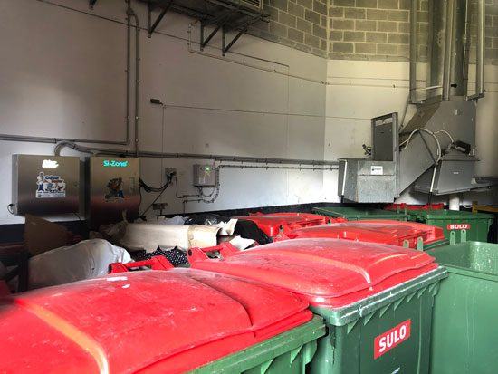 Odour Doctor units on a loading dock wall, above a row of bins and beside the compactor